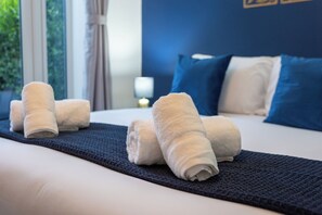 A neatly made bed with rolled white towels and a dark blue bed runner.