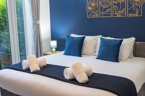 A neatly made bed with white and blue pillows, a dark blue bedspread, and two rolled towels on the bed. - Pleasant Studio in St Albans (St Albans)