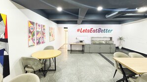 Un espace de bureau moderne doté d’un coin cuisine, d’une table ronde et d’œuvres d’art colorées accrochées aux murs.