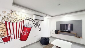 Un salon moderne doté d’un grand téléviseur à écran plat, d’un fauteuil poire, d’une table basse blanche et d’une fresque murale représentant des grains de maïs.