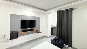 Un salon moderne avec un téléviseur à écran plat fixé à un mur gris, une table basse blanche et un fauteuil en forme de sac noir.