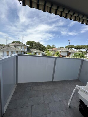 A rooftop terrace with a tiled floor, white walls, and a view of neighboring houses and trees.