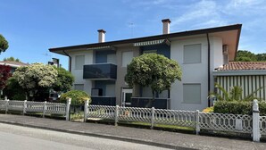 A two-story building with a flat roof, a balcony, and a white picket fence. - Comfortable Flat Near the Beach and Luna Park (San Michele al Tagliamento)