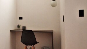 Una habitación pequeña y minimalista con un escritorio, una silla, una lámpara colgante y un cubo de basura.