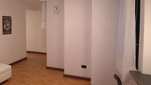 Amplia habitación con suelo de madera, paredes blancas y un ventanal con cortinas translúcidas.