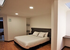Una habitación de hotel moderna con una cama grande, cabecera oscura y una mesita de noche pequeña.