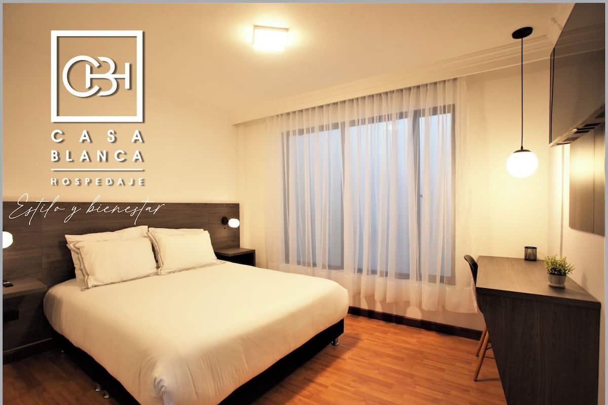 Ein Hotelzimmer mit einem großen Bett, einem Schreibtisch und einem Fenster mit transparenten Vorhängen.