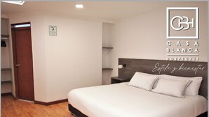 Una habitación de hotel con cama, suelo de madera, mesita de noche y estante en la pared.