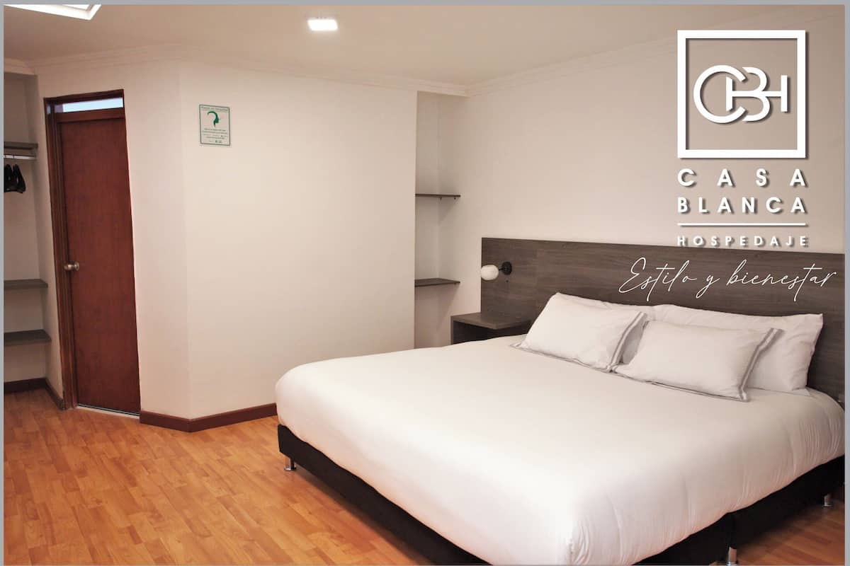 Ein Hotelzimmer mit einem Bett, Holzboden, einem Nachttisch und einem an der Wand befestigten Regal.