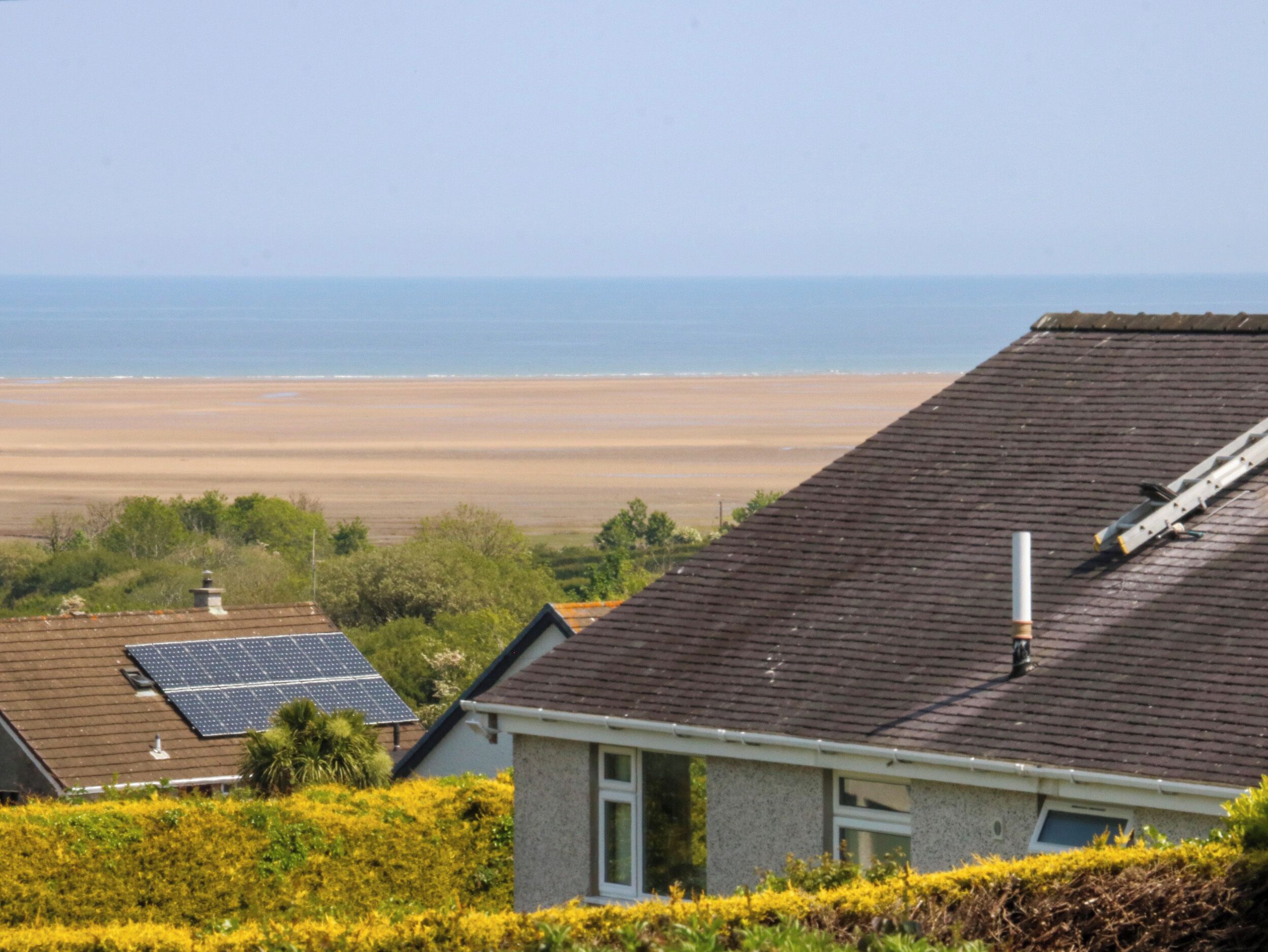 A residential area with houses, solar panels, and a beach in the background.