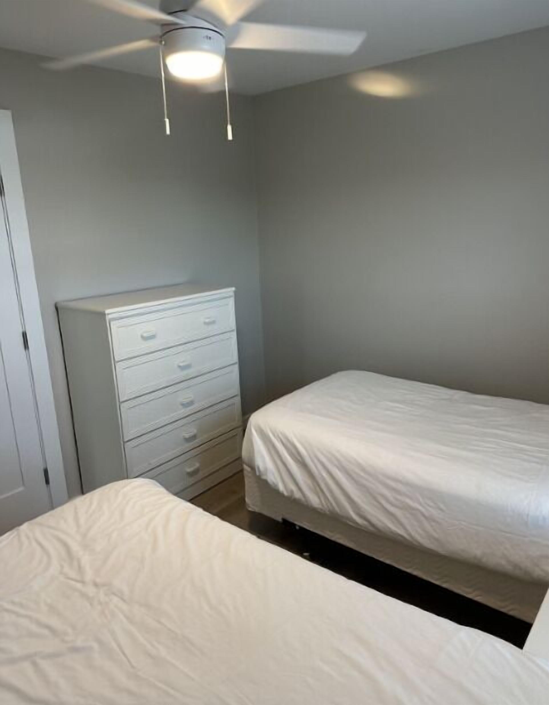 A bedroom with a bed, a dresser, and a ceiling fan.