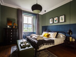 Une chambre à coucher avec un lit, une commode, une fenêtre donnant sur un beau paysage et un mur orné de tableaux.
