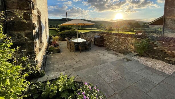 Eine Terrasse mit Steinmauern, einem Tisch, Stühlen und einem Grill.