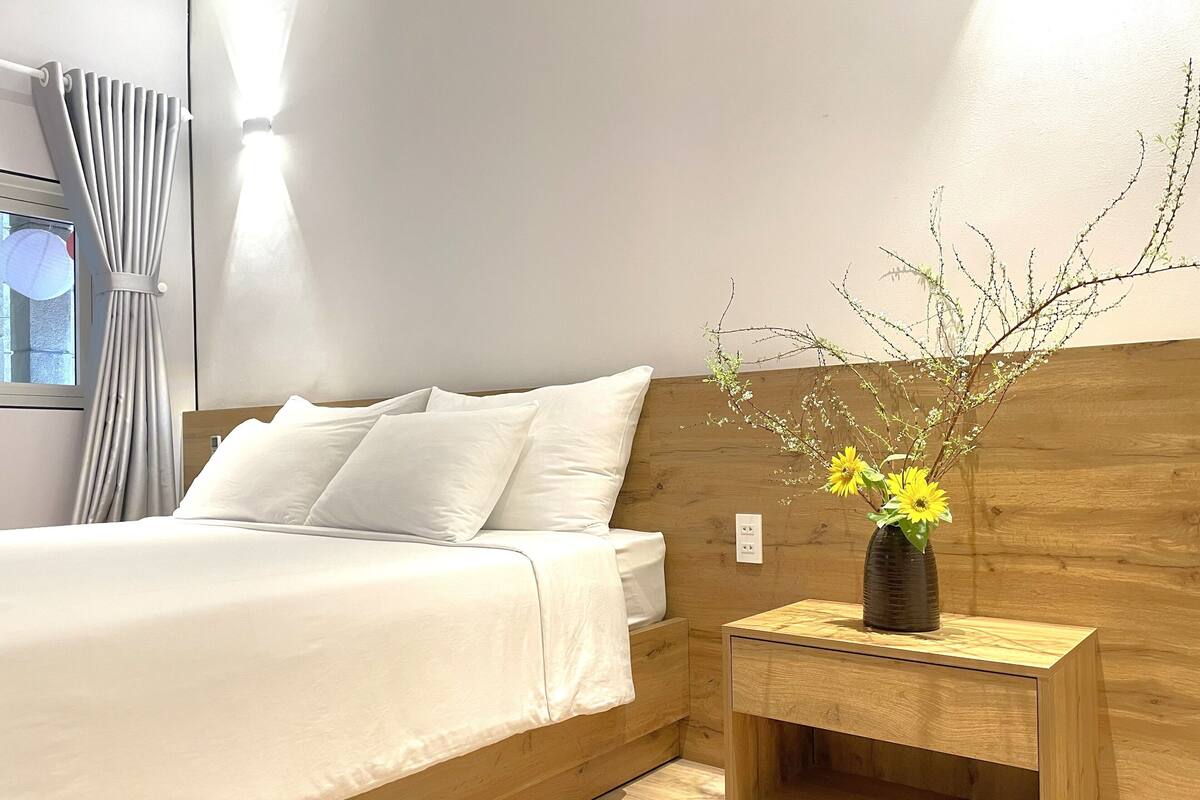 A modern bedroom with a wooden headboard, a bed with white linens, and a nightstand with a vase of flowers.