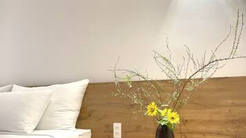 A bedroom with a wooden headboard, a bedside table with a vase of flowers, and a wall-mounted light fixture.