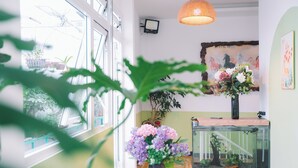 A room with a large window, a potted plant, a vase with flowers, a fish tank, and a wall-mounted TV. - Gold House (Xuan Huong - Da Lat)