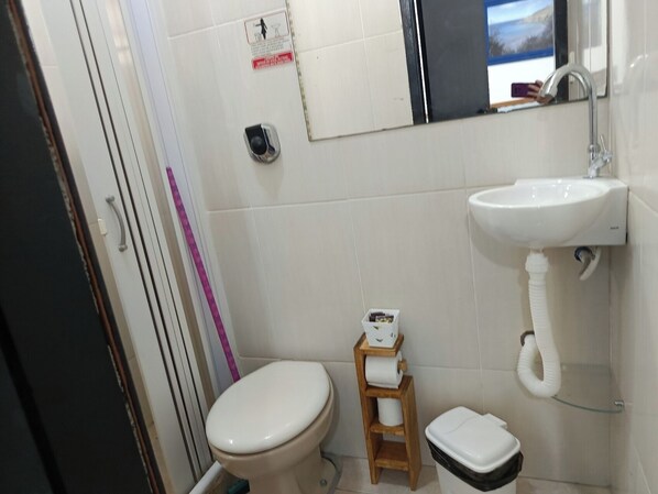 A small bathroom with a toilet, a sink, and a mirror. - Suítes e Kits da Natasha (Arraial do Cabo)