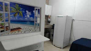 A room with a beach view through a window, a white counter, a refrigerator, and a gas cylinder. - Suítes e Kits da Natasha (Arraial do Cabo)