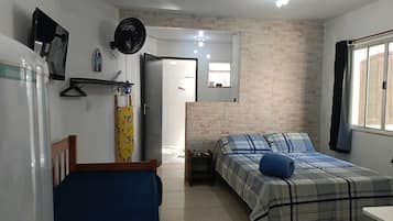 Un dormitorio con cama, mesita de noche, ventilador de techo y ventana con cortinas.