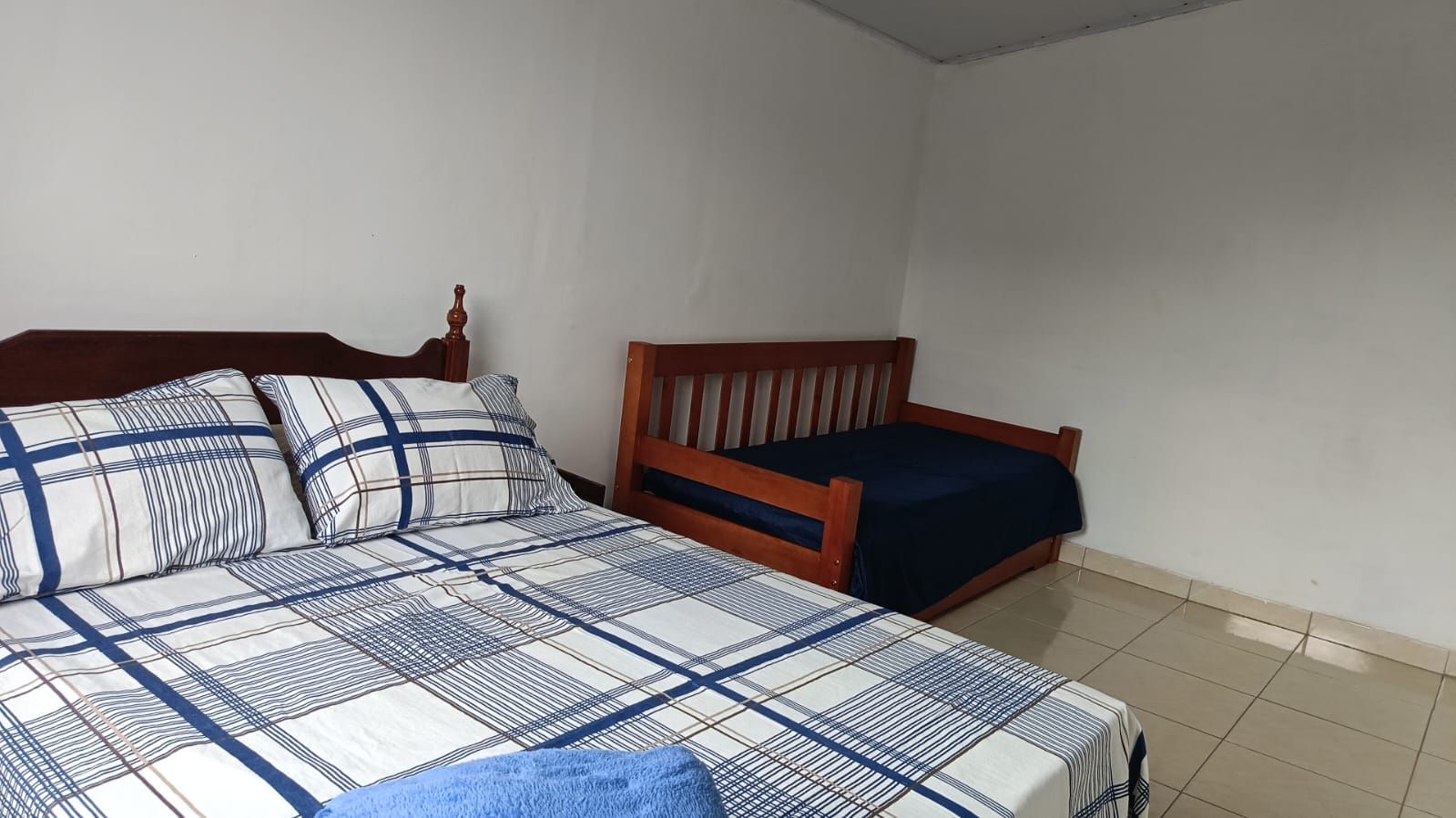 A bedroom with two wooden beds, one with a blue bedspread and the other with a dark blue bedspread.