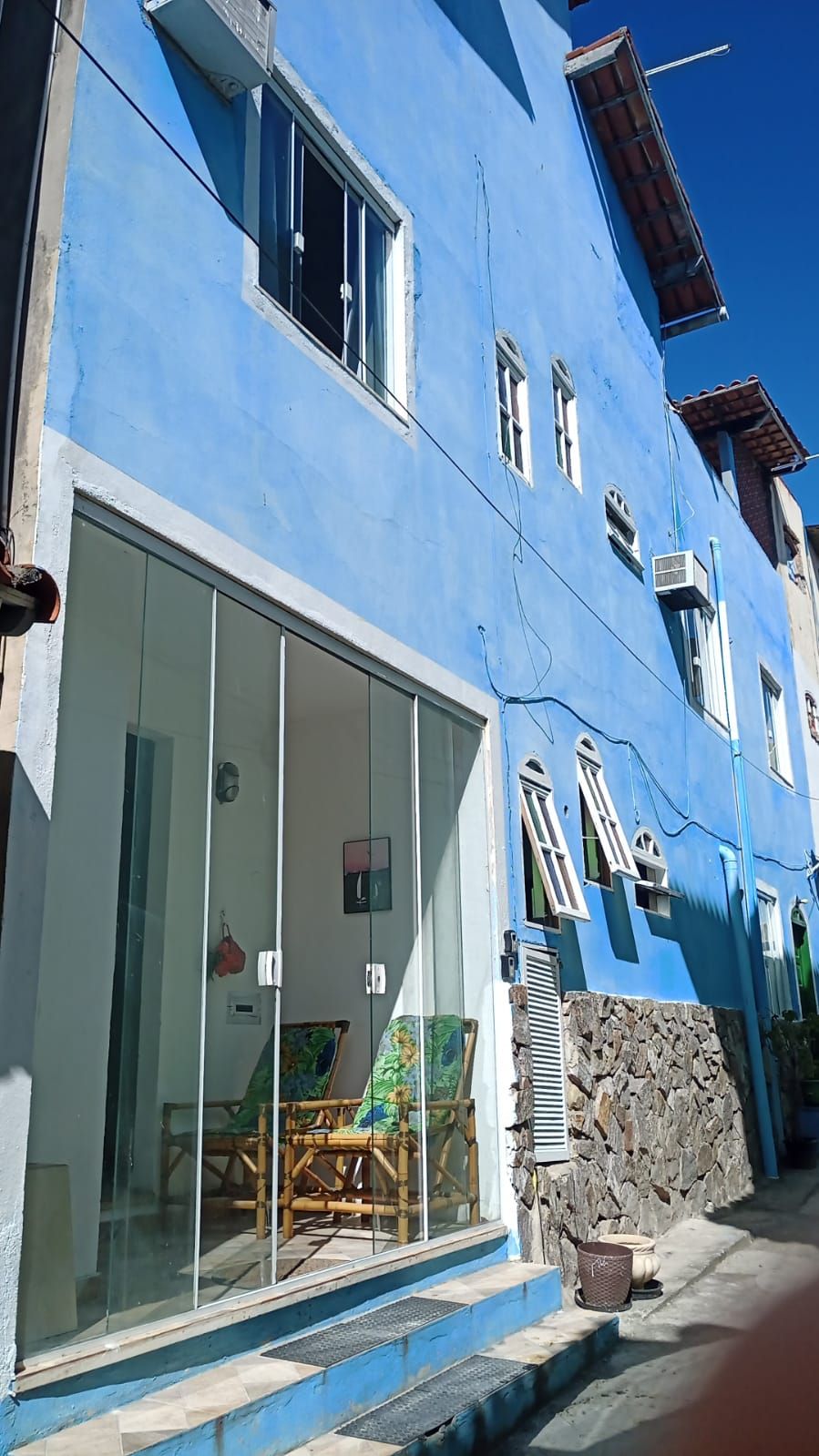 Un edificio azul con un amplio acceso por puerta de vidrio, una pared de piedra y una pequeña zona de estar al aire libre.