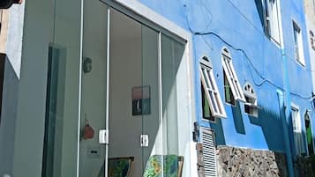 Un edificio azul con un amplio acceso por puerta de vidrio, una pared de piedra y una pequeña zona de estar al aire libre.