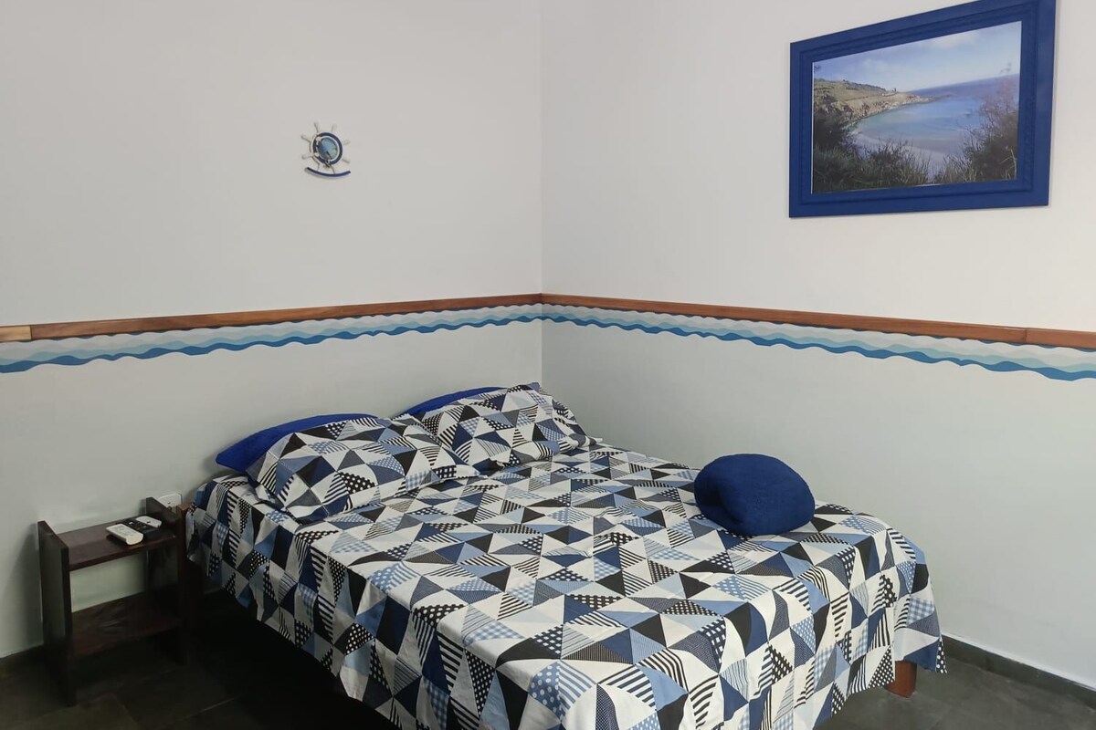 A bedroom with a bed, a nightstand, a wall clock, and a framed picture.