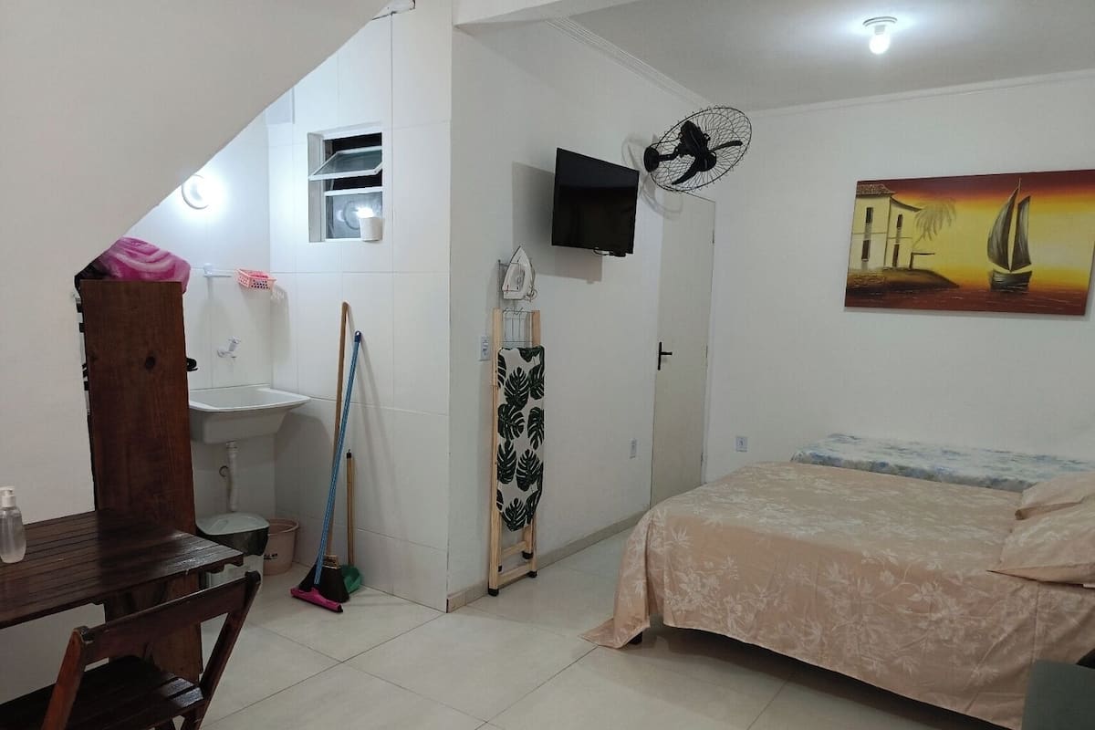 Un dormitorio con cama, televisor, un cuadro, una ventana y un baño con lavamanos.