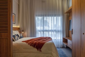 A bedroom with a bed, a TV, a wooden wardrobe, and a large window with sheer curtains. - Akile Cardoso de Almeida (Sao Paulo)
