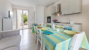A modern kitchen with white cabinets, a dining table set with plates and cutlery, and a sofa in the foreground. - Villetta Soave - Santo Isidoro (Santo isidoro)