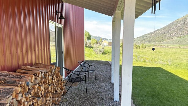 A covered outdoor area with a gravel floor, wooden logs stacked on the left, and a metal chair. - Charming 3-bedroom barn with AC, WiFi in delightful Lava Hot Springs (Lava Hot Springs)