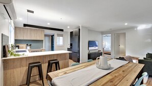 Een moderne keuken met houten kasten, een centraal eiland en een eethoek met een tafel en stoelen.