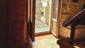 A room with a stone wall, a wooden dresser, a woven mat, and a balcony with a view of a hill. - Arco-Navarra Rural House (Artariáin)