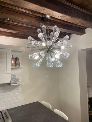 Un espace repas agrémenté d’un lustre moderne, de murs en briques blanches et d’une poutre en bois au plafond.