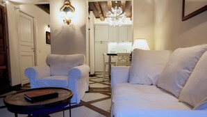 Una habitación con un sofá blanco, un sillón blanco, una mesita redonda con un libro y una araña.