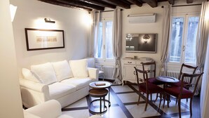 Un salón con un sofá blanco, una mesita redonda y un comedor con mesa y sillas.