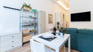 Een moderne woonkamer met een witte eettafel, een blauwgroene bank en een ingebouwde boekenkast met servies en decoratieve objecten.