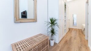 Een gang met een houten bankje, een potplant en een spiegel aan de wand.