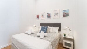 Een keurig opgemaakte slaapkamer met een bed, nachtkastjes en wanddecoraties met afbeeldingen van bekende steden.