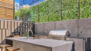 An outdoor kitchen with a built-in grill, bar stools, and a concrete backsplash.