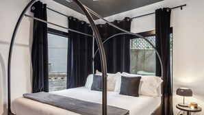 A modern bedroom with a bed, a ceiling fan, a nightstand, and a view of the city.