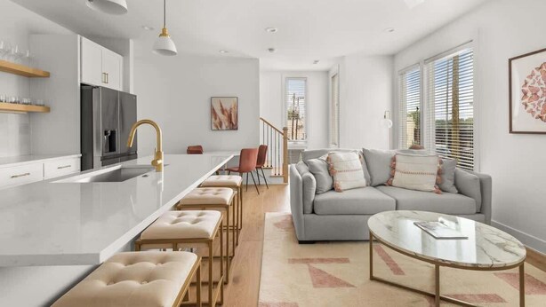 A modern kitchen with a central island, a dining area with chairs, a grey sofa, and a coffee table.