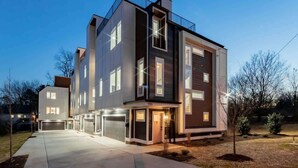 A modern multi-story residential building with a garage, large windows, and a well-lit entrance.