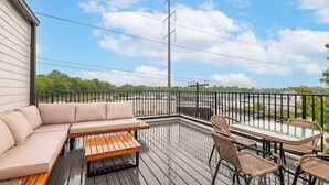 A covered outdoor deck with a sofa, table, and chairs, overlooking a parking area and greenery.
