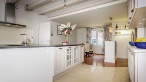 Een moderne keuken met witte kasten, een centraal eiland en een eethoek met een tafel en stoelen.