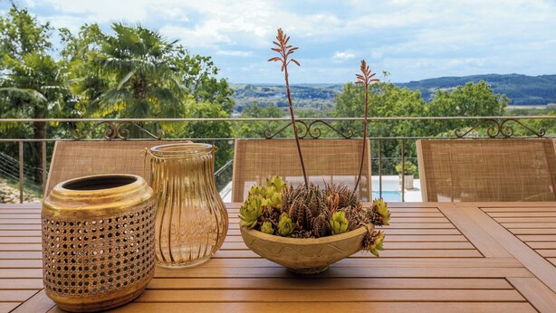 Een houten tafel met twee gevlochten vazen en een schaal met vetplanten op een balkon met een mooi uitzicht.