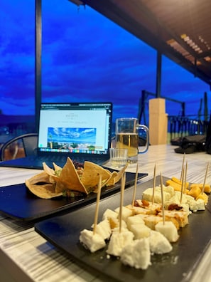 Una mesa de comedor con una laptop mostrando una página web, una jarra de cerveza y un plato de aperitivos que incluyen queso y totopos.