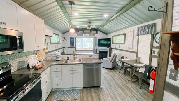 Una cocina compacta con microondas, estufa, lavaplatos y un pequeño comedor con una silla y una mesa.
