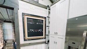 Una cocina con un refrigerador de acero inoxidable, un dispensador de agua y una pizarra con escritura.