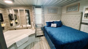 Un dormitorio con una cama grande, cabecera, ventana con cortinas, mesita de noche y espejo.